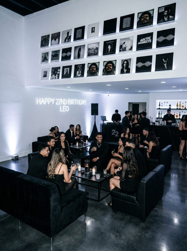 Monochromatic vinyl gallery birthday setup with black seating and white walls.